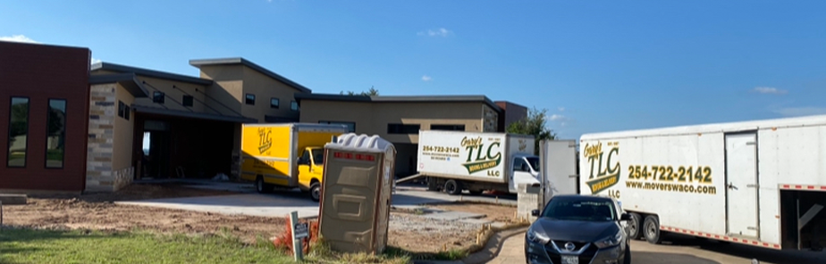 Commercial warehouse facility with yellow and white TLC delivery trucks parked outside