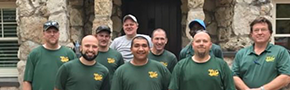 Team of eight people in green shirts standing together in front of a stone building