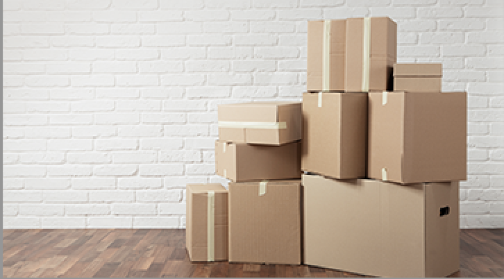 Stack of various cardboard moving boxes against white brick wall