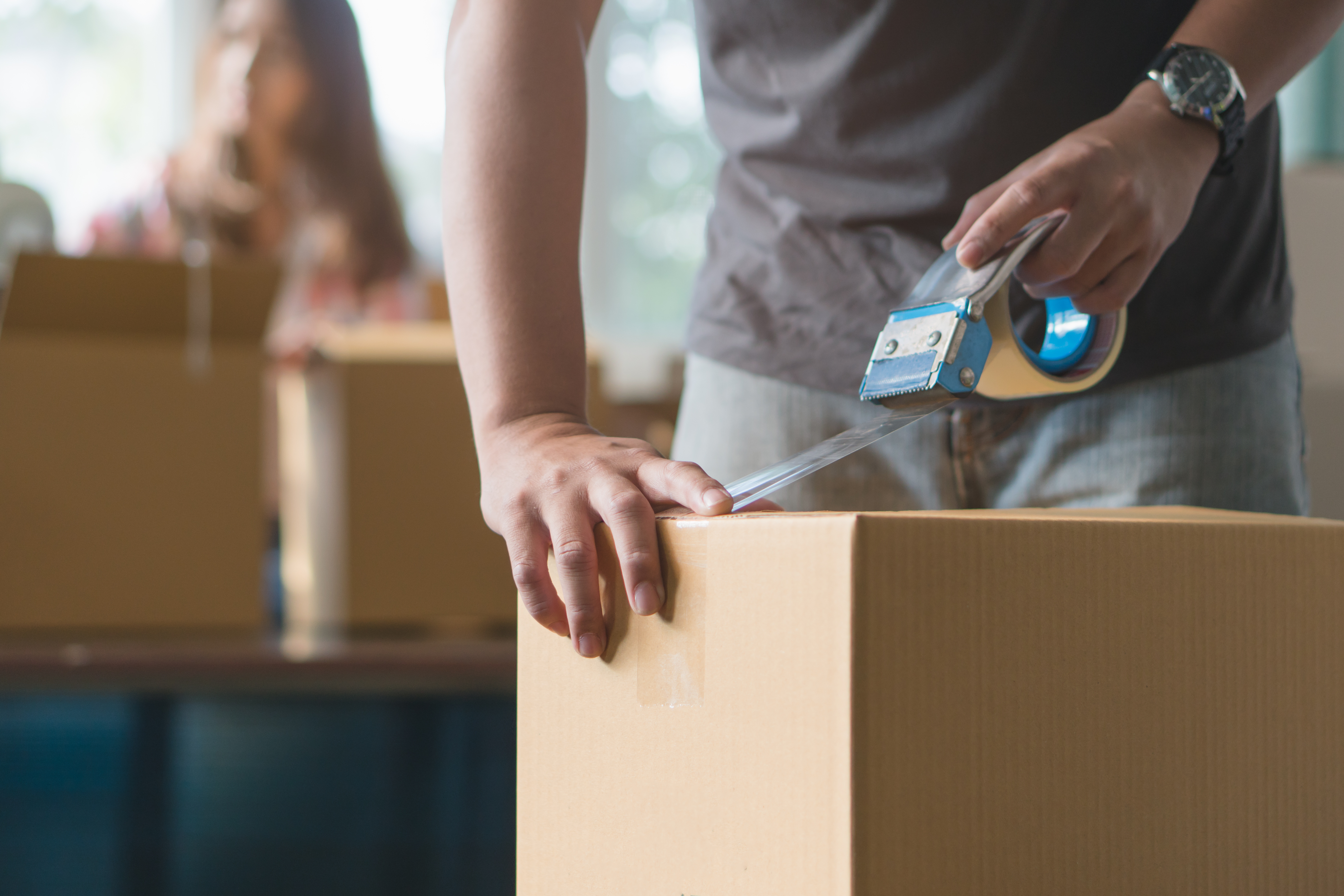 Worker sealing a cardboard box with packing tape in a warehouse